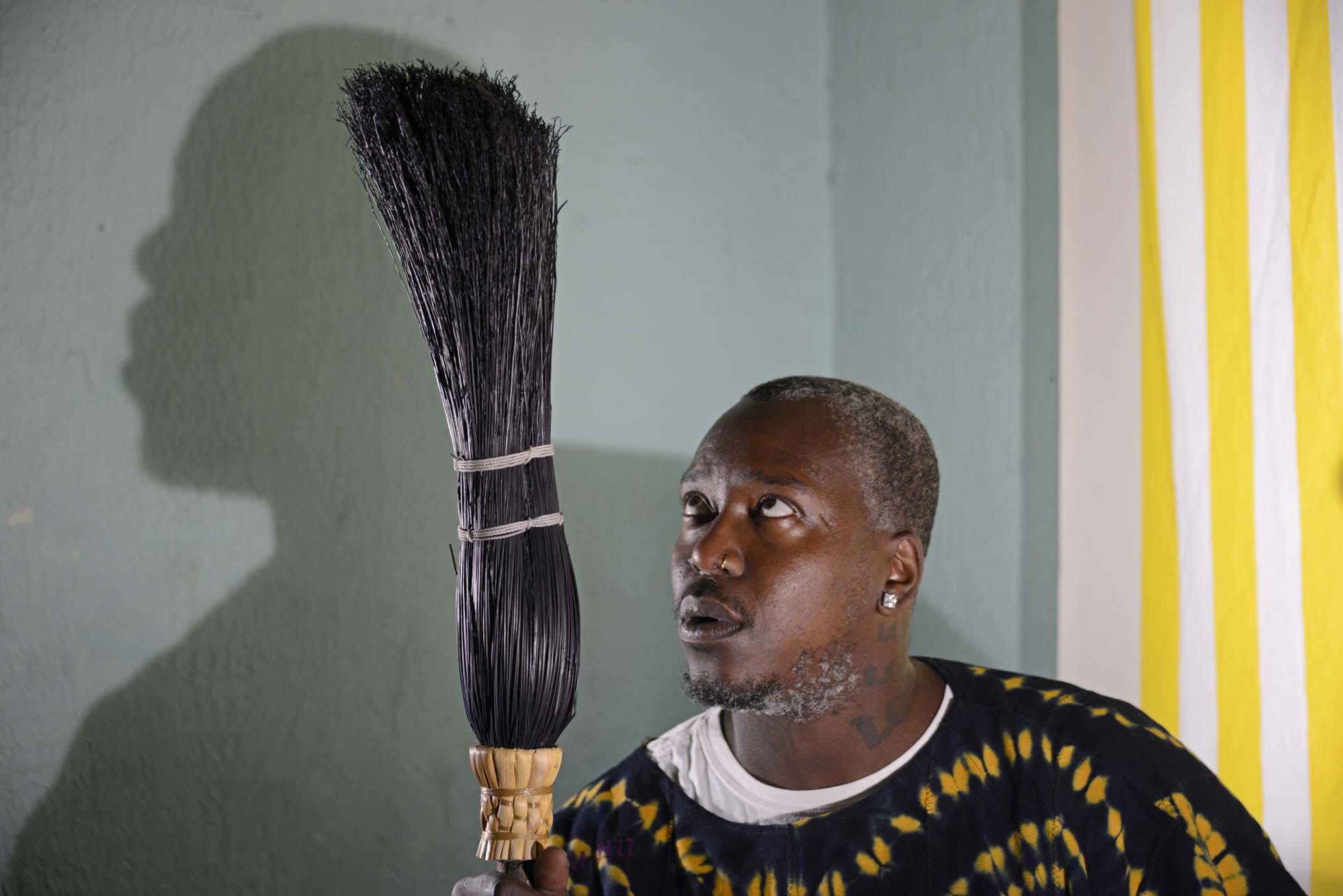 Brontez Purnell sits in his study/studio/altar room in his home in Oakland, CA on October 19, 2020. He’s holding a broom that he keeps there. In his words, “My family is just really superstitious and witchy and they said if you sleep with a broom in the room ghosts won’t bother you because ghosts are really nosy, hence why they haunt people. But ghosts will be too busy counting the bristles on the broom to disturb your sleep.”