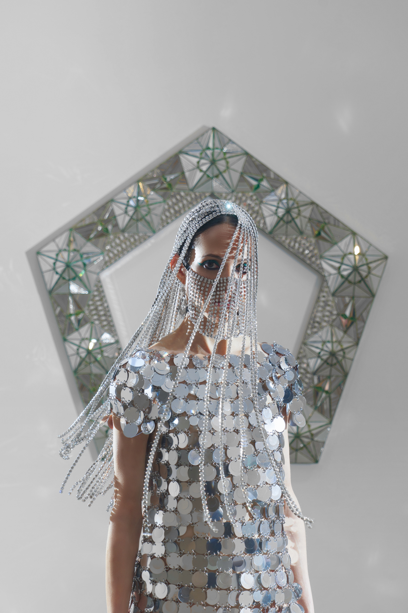 Makeup by Tomomi Sano. Hair by Rochelle Walker. Monir Shahroudy Farmanfarmaian, <em>Fifth Family Pentagon</em>, 2014. Chain-disc mini dress by Paco Rabanne. Crystal hairpiece and crystal fringe mask accessory by Area.