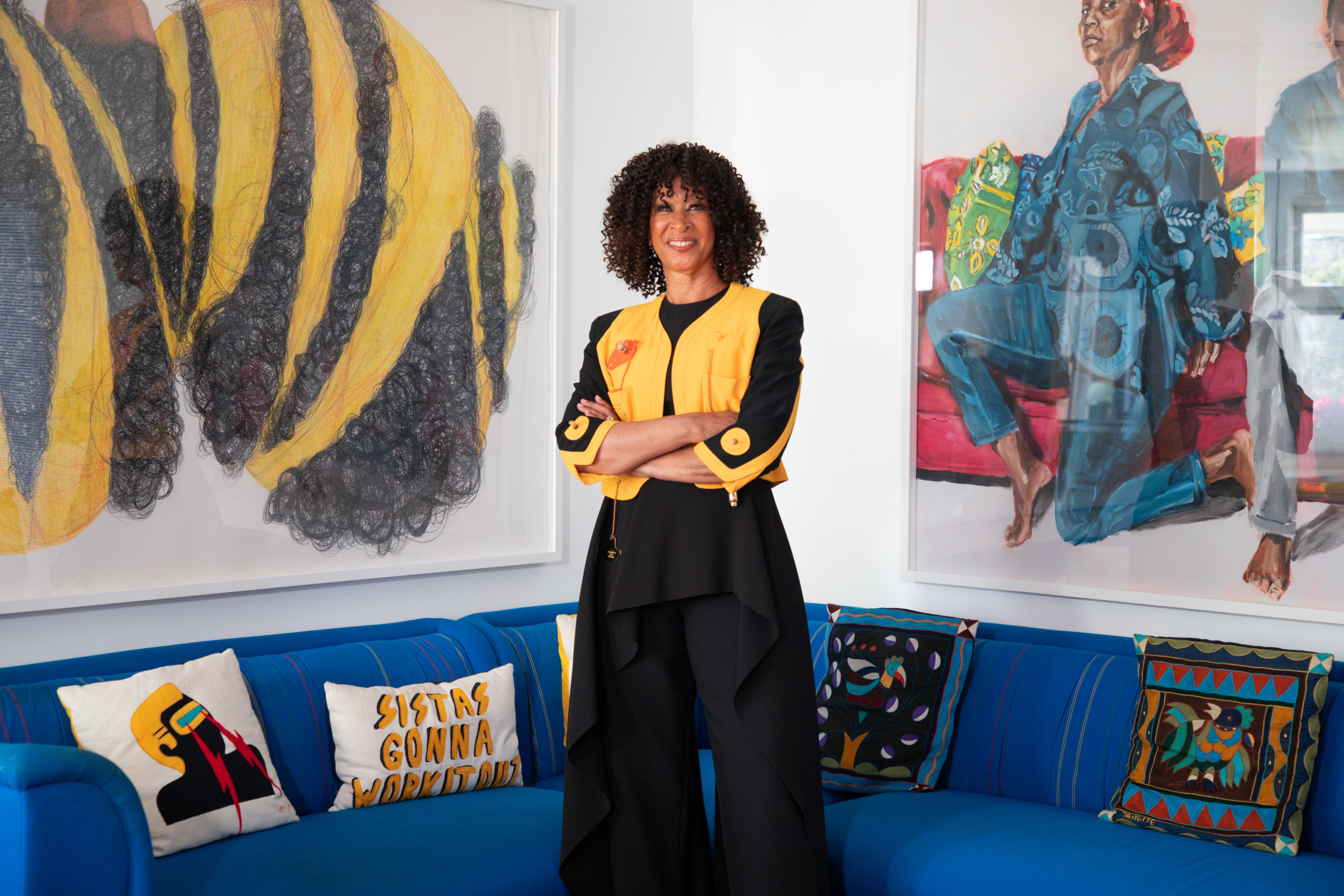 Joy Simmons wearing vintage Moschino Lifesaver jacket and flanked by Mequitta Ahuja's Bundle, 2008, on the right and Wangari Mathenge's The Ascendants, 2019, at home in Los Angeles.