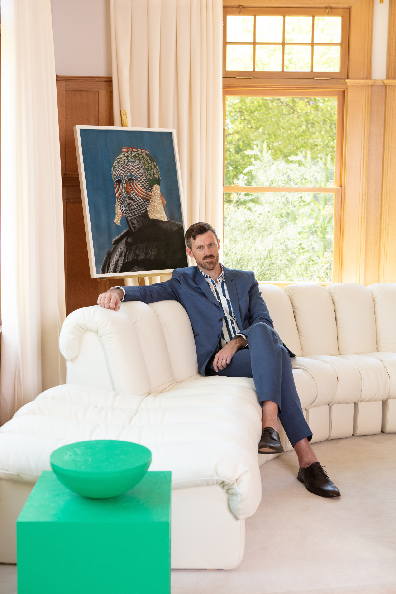 chet callahan in his home on white couch with blue portrait painting and window behind him