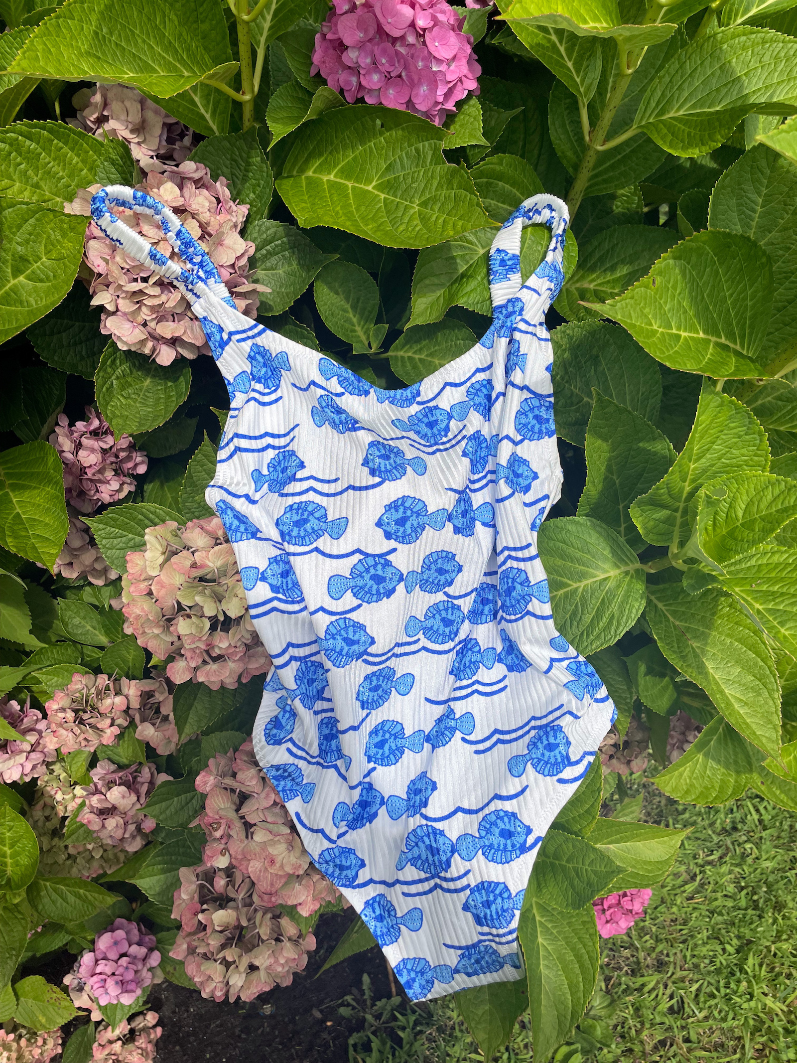 one piece in white with blue fish pattern by fisch swim resting on hydrangea bush