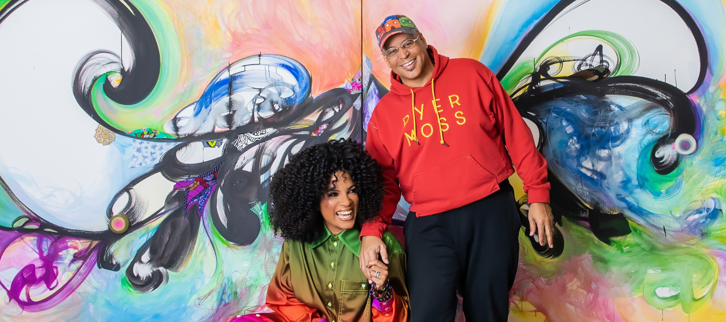 Janine Sherman Barrois and Lyndon Barrois smile in front of a colorful painting.