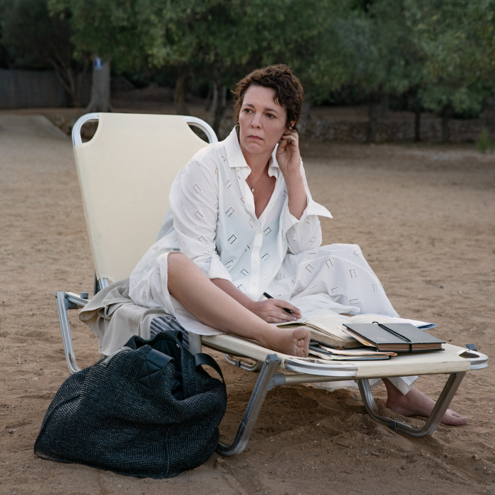 Olivia Colman acting as Leda sits on the beach in a loungechair.