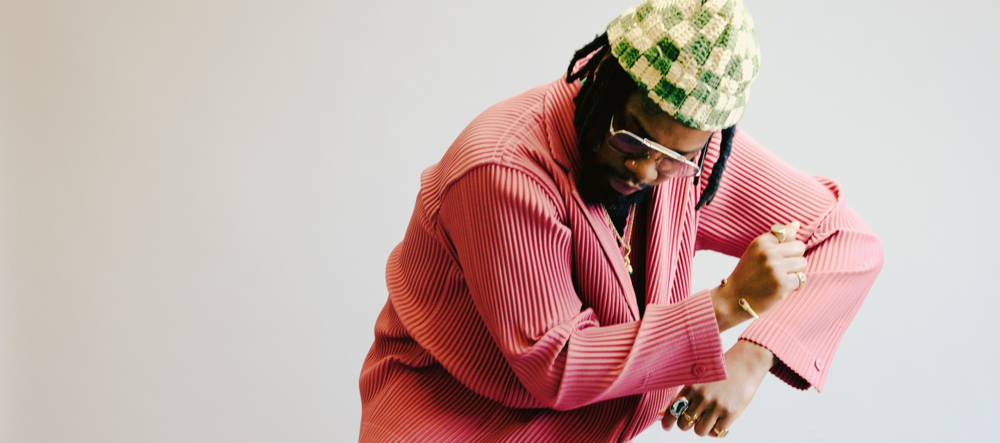 serpentwithfeet dances in front of the camera in a pink outfit and green checkered beanie.