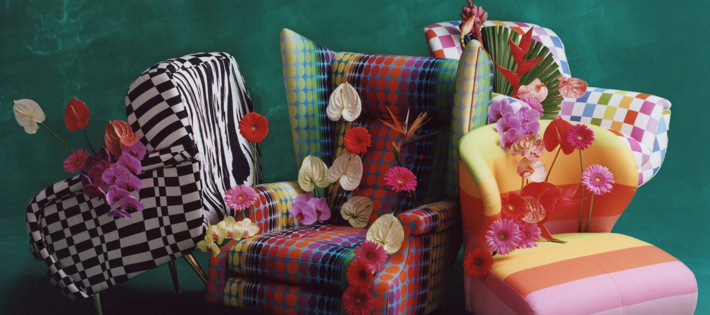 Four colorful chairs with different patterns, decorated with flowers against a dark green backdrop.
