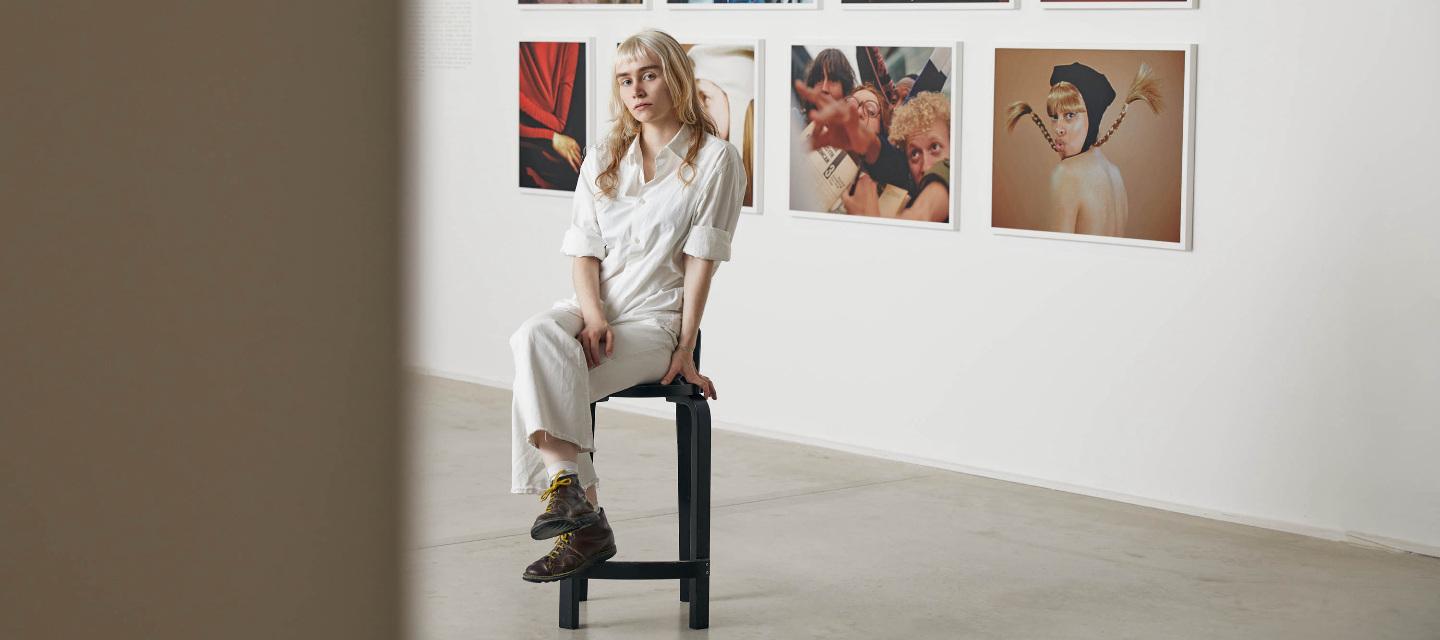 woman on stool in front of photographs