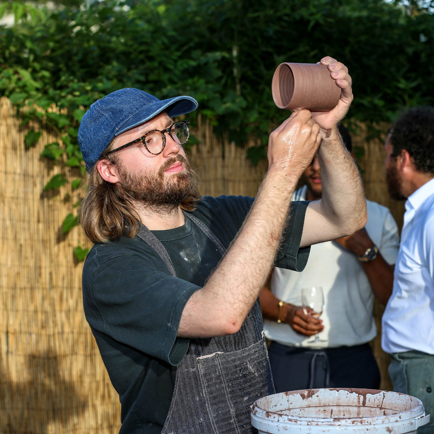 artist looks at one of his ceramic pieces, a mug, at outdoor party