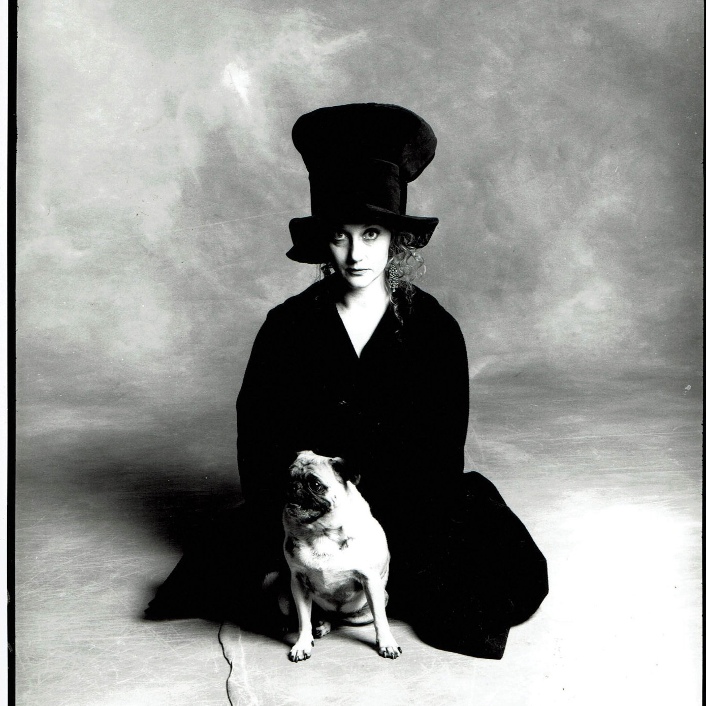 a Woman sitting with a dog and a large hat.