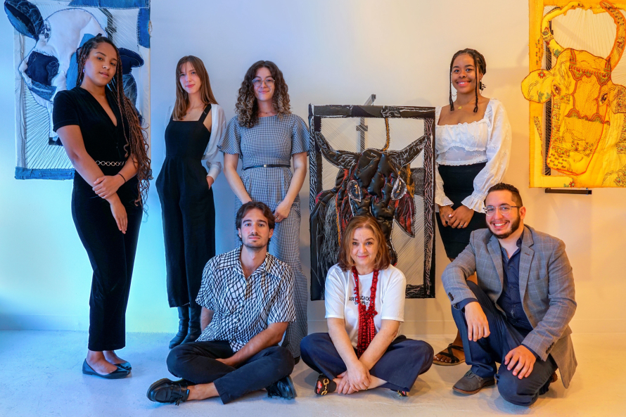 The CAMP Gallery staff sit and stand in front of a piece of art