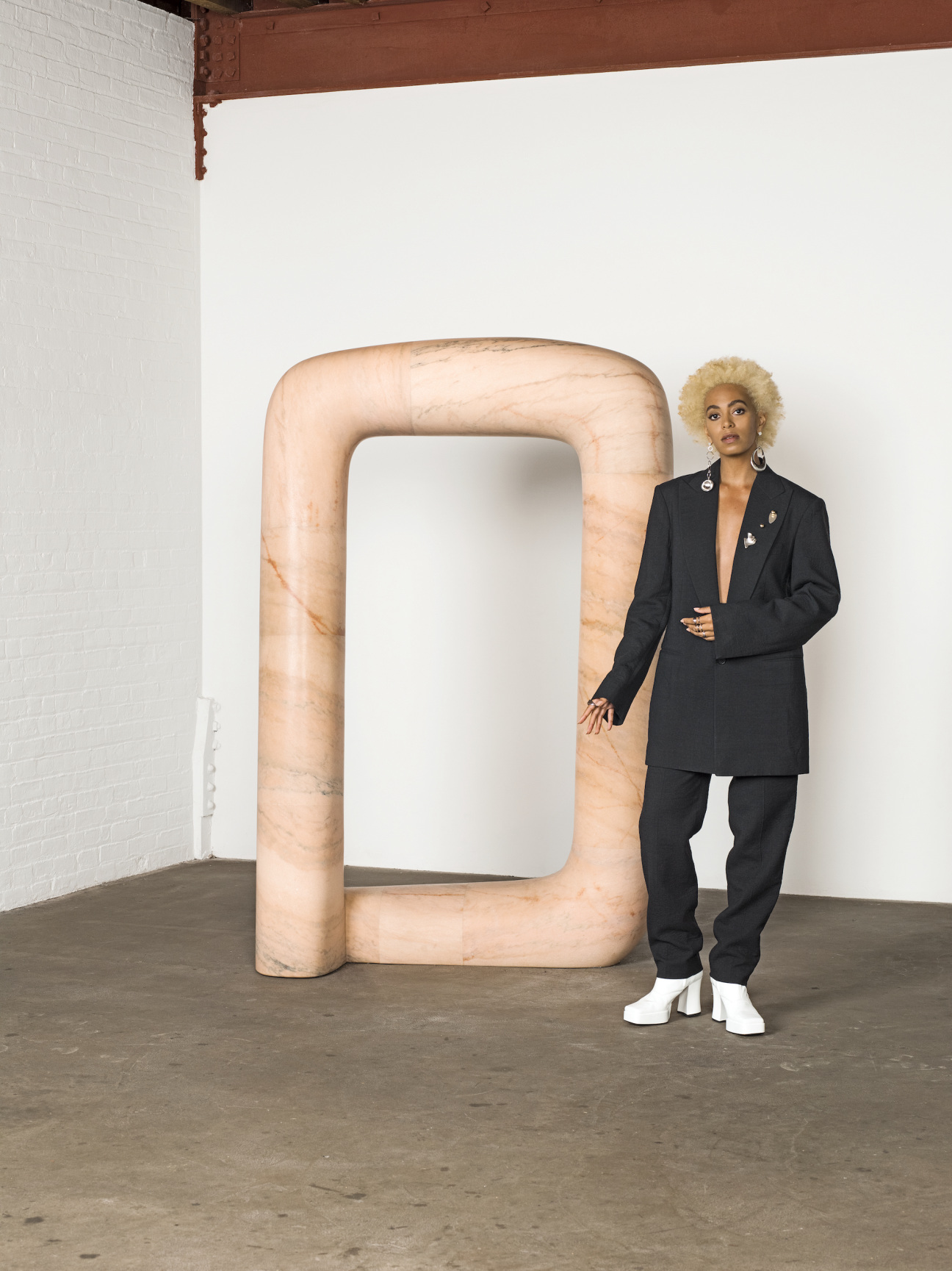 solange posing in oversized suit to the right of a square shaped sculpture