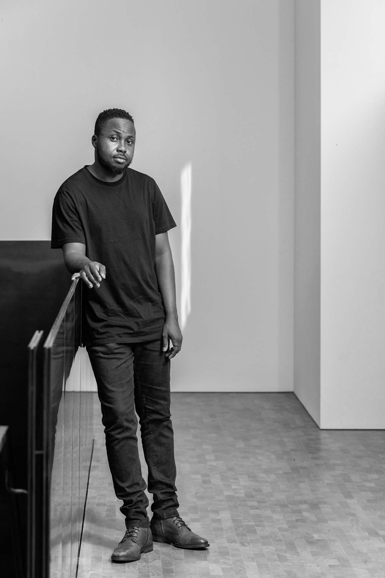 Black man leaning against furniture. Image in black and white.