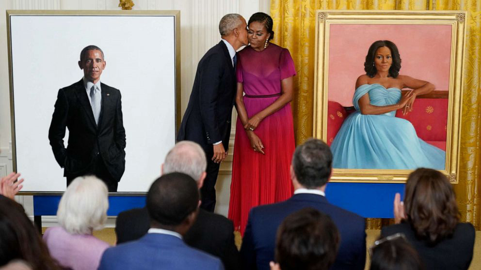 Michelle and Barack Obama standing in front of their Official White House portraits.