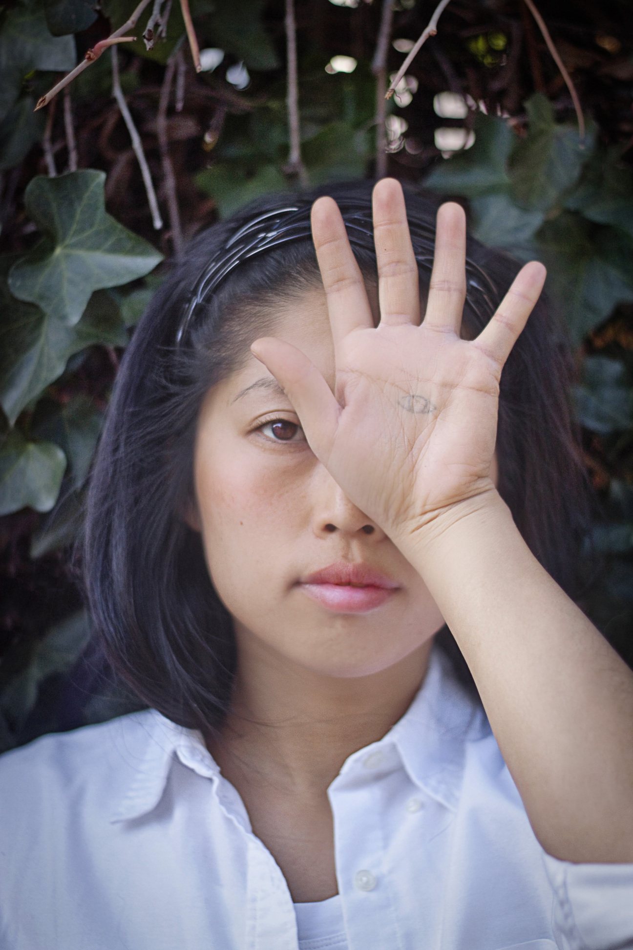 Naoco Wowsugi, with a hand covering part of her face, looking at the camera.